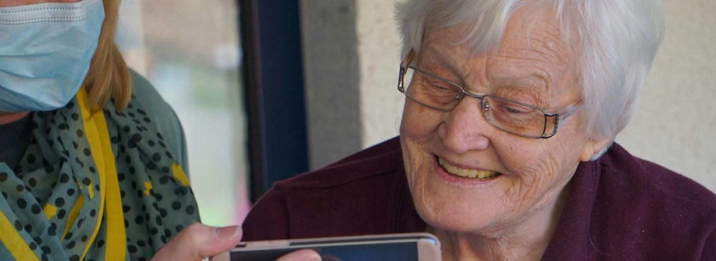 A volunteer holding a smartphone for an older patient to view the screen