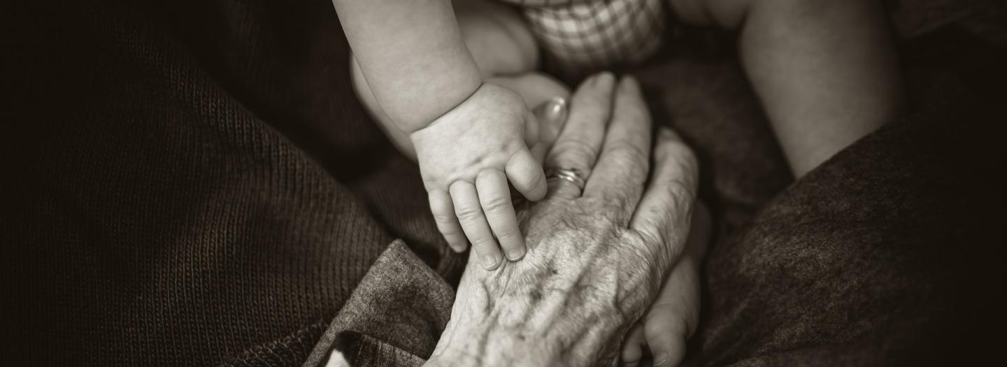A baby's hand atop an elderly's hand